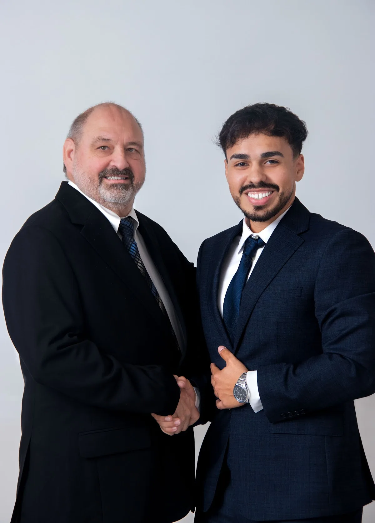 Carlos A. Diaz and Giovanni J Garcia of Icon Premier Group standing together in dark suits and ties against a plain light studio wall