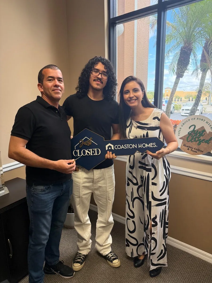 Three people at a closing holding a house-shaped Closed sign from Coaston Homes in a sunlit office