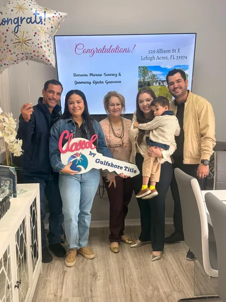 A family with a small child in front of a screen reading Congratulations at their Gulfshore Title closing, holding a Closed sign