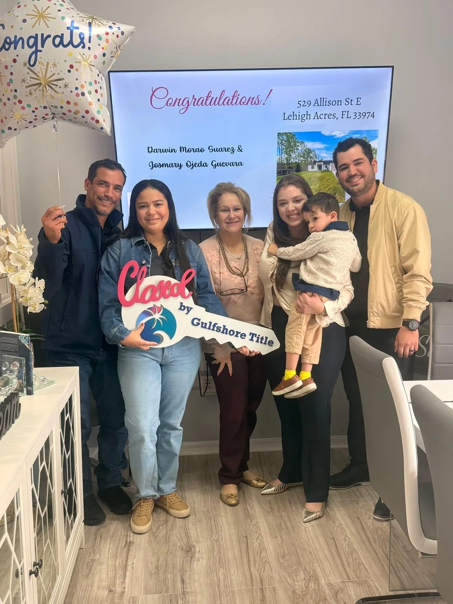 A family with a small child in front of a screen reading Congratulations at their Gulfshore Title closing, holding a Closed sign