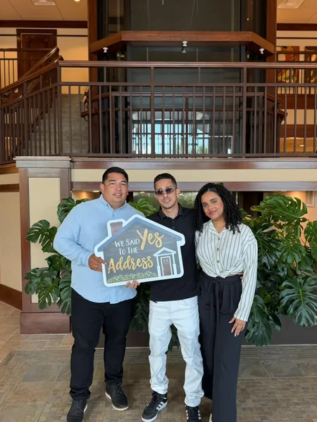 Three people in a title company lobby holding a house-shaped We Said Yes To The Address sign