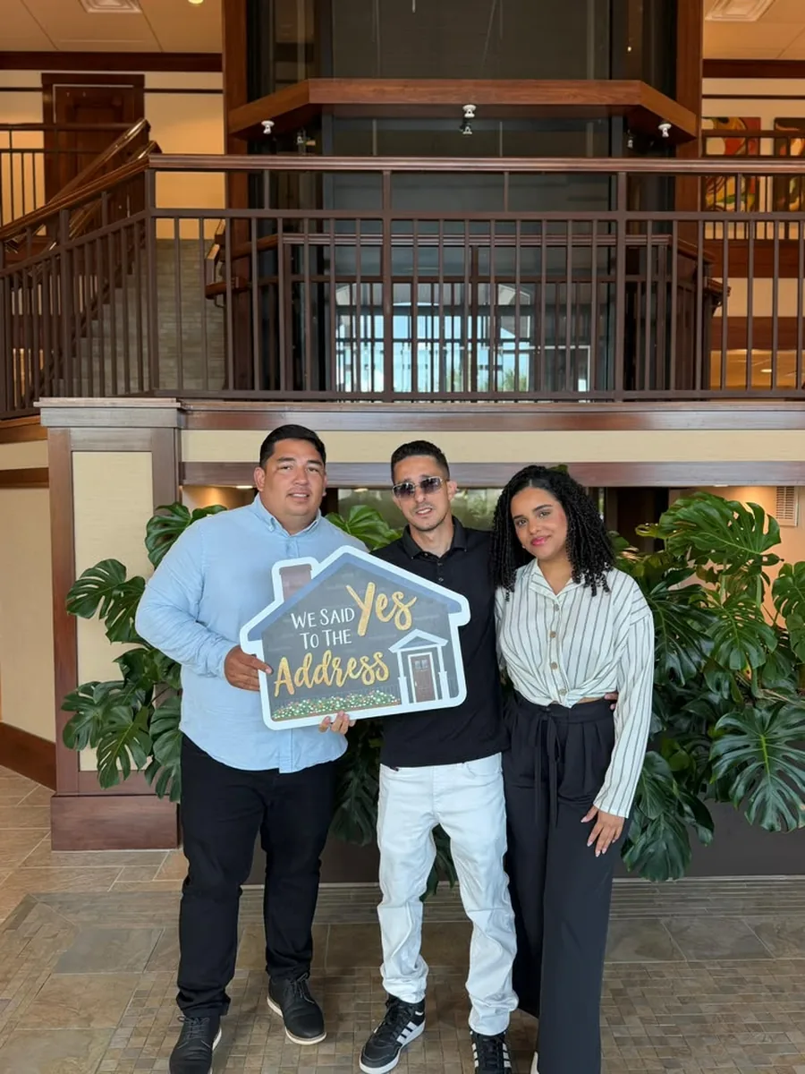 Three people in a title company lobby holding a house-shaped We Said Yes To The Address sign