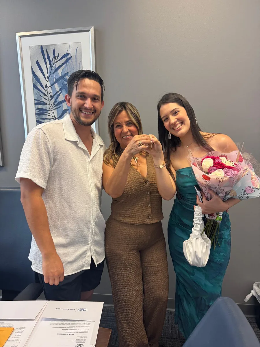 Three people in an office celebrating a closing, one holding a bouquet of flowers
